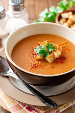 Red lentil cream soup with croutons in bowl on wooden table