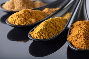 Small black bowls of Indian spices on black reflective background .