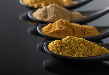 Small black bowls of Indian spices on black reflective background .