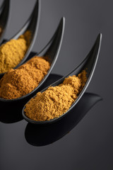 Small black bowls of Indian spices on black reflective background .