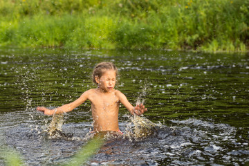 Adorable curly baby girl splashing in a beautiful river on a sunny summer day