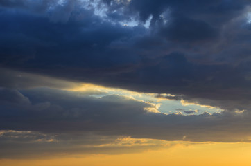 the rays of the sun setting beyond the horizon break through the gray clouds and illuminate them with shades of different colors