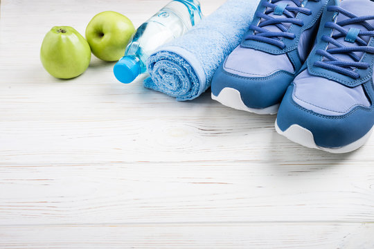 Flat lay sport shoes, bottle of water, apples, towel and earphones on white wooden background. Sport equipment. Healthy lifestyle, sport and diet concept. Copy space