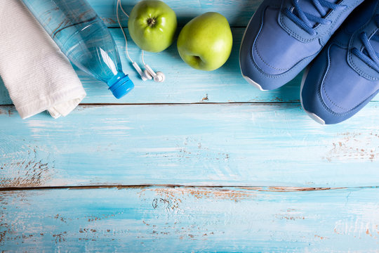 Flat lay sport shoes, bottle of water, apples, towel and earphones on blue background. Sport equipment. Healthy lifestyle, sport and diet concept. Copy space, top view