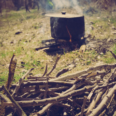 Big touristic cauldron with soup on burning campfire in the forest, image with warm vintage toning