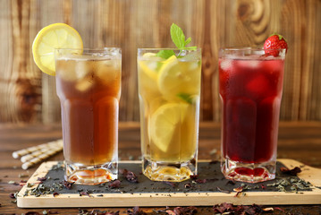 Three glasses of different cold tea drinks black, green with lemon and mint, hibiscus teas.