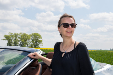 Beautiful happy brunette woman with sunglasses with her new Luxury Convertible Sports Car on a sunny day