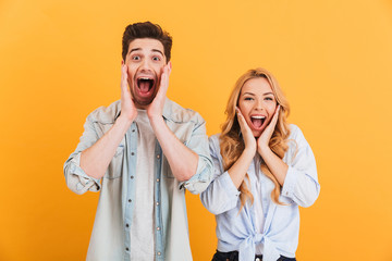 Image of ecstatic people man and woman in basic clothing screaming in surprise or delight and touching cheeks, isolated over yellow background - obrazy, fototapety, plakaty
