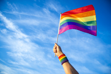 Colorful backlit rainbow gay pride flag being waved in the breeze against a sunset sky. - 204967511