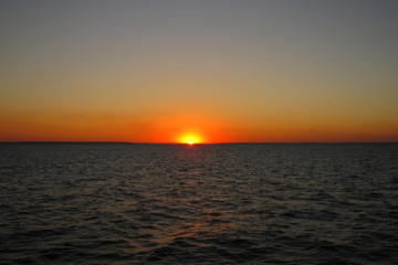 Naklejka premium Beautiful orange sunset on the lake in summer against the setting sun on the horizon and the evening cloudless sky above the water