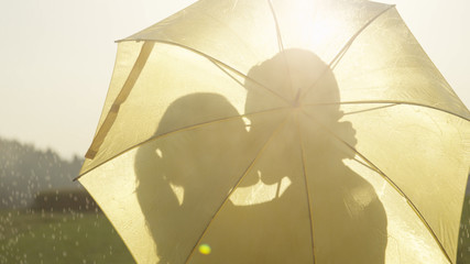 CLOSE UP: Couple hidden behind yellow umbrella kisses while dancing in rain.