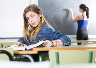 Young girl is sitting at the desk and reading text in the classroom