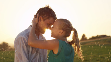 CLOSE UP: Lovely young couple are about to kiss in rain at beautiful sunset.