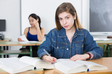 Fototapeta premium Girl is sitting at the desk and writing homework