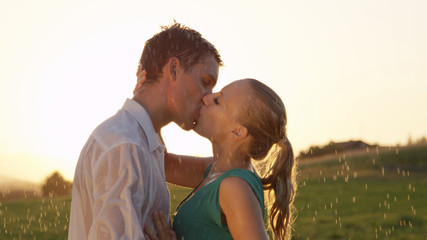 CLOSE UP: Cheerful young man and woman kiss passionately during a spring shower.