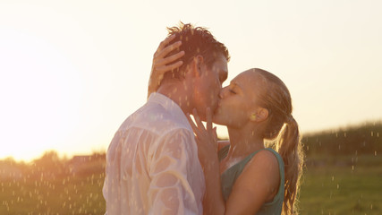 LENS FLARE: Blonde woman caresses boyfriend's face as they kiss in the rain.