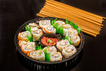 Close up of large set of delicious japanese rolls on a black plastic plate over a wooden table.
