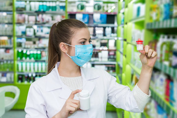 Chemist looking at bottle with pills in drugstore