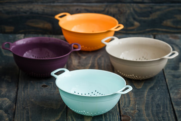 Colorful Plastic Colanders with Handles on Blue Wooden Background