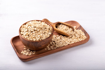 Old fashioned rolled oats in a wooden bowl on white wooden table