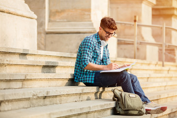 handsome young student standing on stairs of university with his notebooks