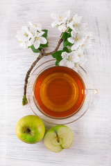 glass of tea with fresh ripe green apple decorated with beautiful apple blossom on white wooden table , rustic food photography with vintage look