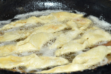 Raw dough is in a frying pan and fried in oil on the fire for pastries and rolls