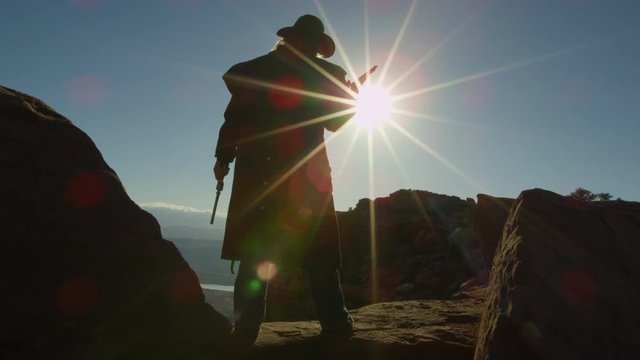 Cowboy standing with guns on desert cliff 