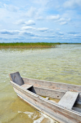 Obraz premium Wooden fishing boat on the lake beach with blue sky, yellow sand and transparent water