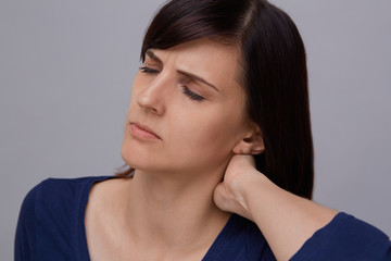 Closeup portrait of young woman on grey background suffering from strong headache, holding hand to nape and closing eyes from pain.Severe migraine.