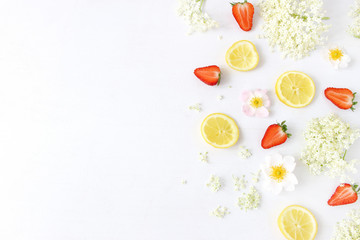 Styled stock photo. Spring or summer fruit composition. Sliced lemons, elderflowers, strawberries and wild roses isolated on white wooden table background. Food pattern. Flat lay, top view.