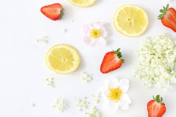 Styled stock photo. Summer fruit composition. Closeup of sliced lemons, elderflowers, strawberries and wild roses isolated on white wooden table background. Food pattern. Flat lay, top view.
