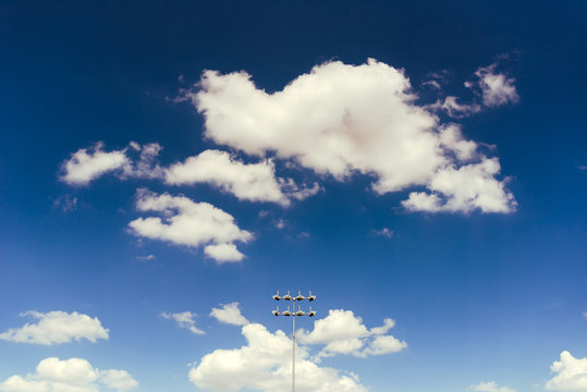 Stadium lights against blue sky with white clodus