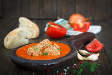 Meatballs in a spicy tomato sauce garnished with fresh aromatic herbs, served with a homemade bread