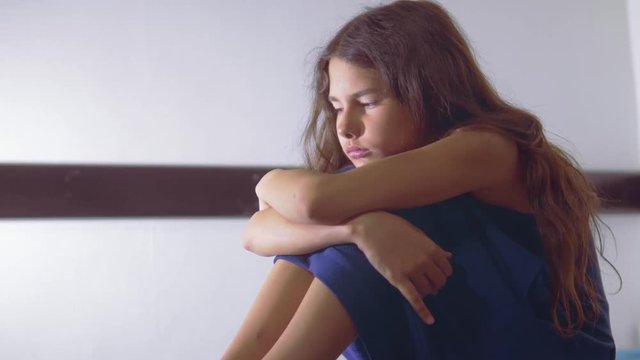 sad girl upset embraces her feet. is depressed and suicidal little lamentable girl schoolgirl sadness misses the night in bed concept childhood family. the problem of education lifestyle in the family