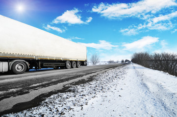 Truck with a trailer on the winter countryside road with snow against sky
