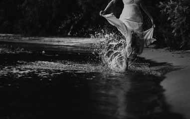 girl in white dress runs on water splashes seashore