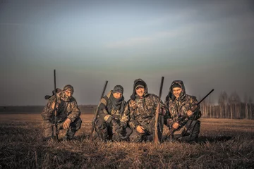 Wall murals Hunting Men hunters group team portrait in rural field posing together against sunrise sky during hunting season. Concept for teamwork  friendship and brotherhood.