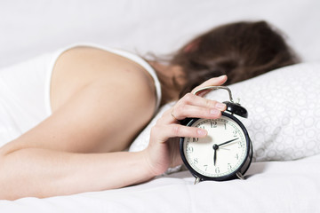 girl is sleeping on bed in bedroom and turns off alarm clock. woman does not want to wake up in...