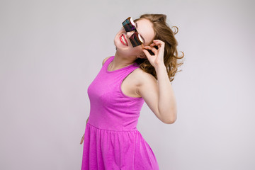 Charming young girl in pink dress on gray background. Cheerful girl in square glasses. The girl adjusts glasses