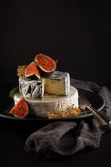 tasty camembert with fresh figs and honey with honeycombs, decorated on a plate on dark background, rustic, moody food photography