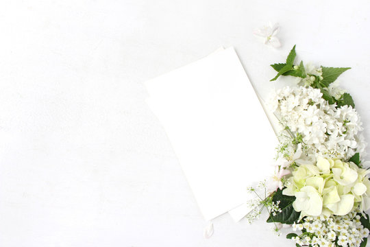 Decorative mockup, floral composition. Wild wedding or birthday bouquet of blossoming white nettle, lilac, apple tree branch, hydrangea, spirea flowers and blank paper cards. Flat lay, top view.