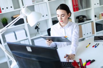 A young girl in the office holds a pen in her hand and works with documents and a computer.