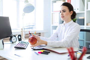 A young girl at the office is working with documents and stretches forth an apple.