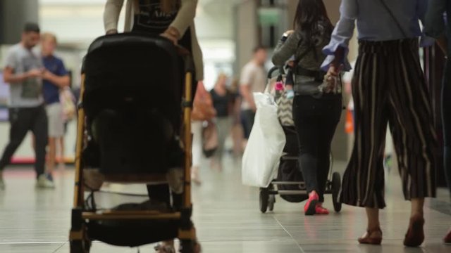 Anonymous young mothers shopping in a mall, walking and pushing strollers.