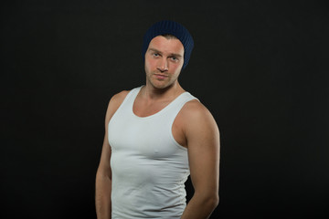 Man with muscular arms and tight T shirt. Macho on confident face with strong muscles look brutal, black background. Man in hat and sleeveless undershirt looks attractive . Masculinity concept