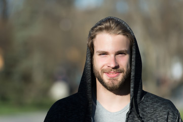 Guy with beard smile in hood on sunny day. Bearded man wear casual sweatshirt outdoor. Fashion macho smiling in stylish sportswear. Lifestyle for active and healthy man, sport