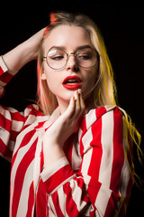 Elegant blonde girl with red lips, wearing glasses, posing with red and yellow light at studio