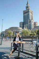 The girl is sitting at a coffee table in the business center of Warsaw. A business woman is waiting for a meeting in Warsaw near the Palace of Culture and Science.