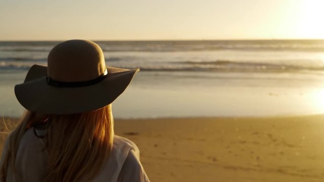 Attractive blond woman walking on the beach at sunset. Slow Motion.